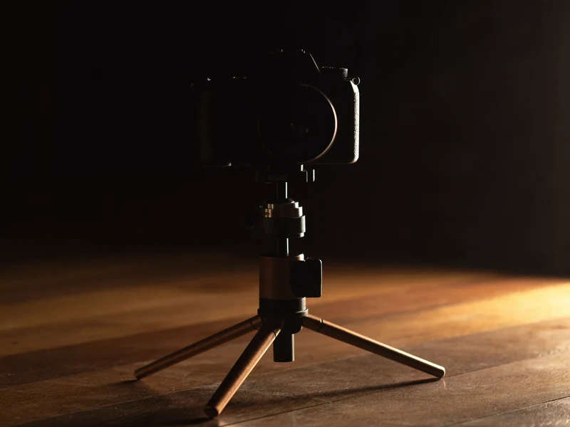 Kamera auf Stativ im dunklen Studio, von einem warmen Konturlicht umrissen