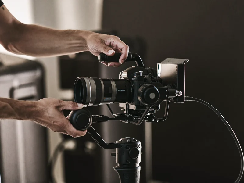 Hände justieren ein Cage-Rig mit Gimbal und Monitorgehäuse in gedämpftem Licht